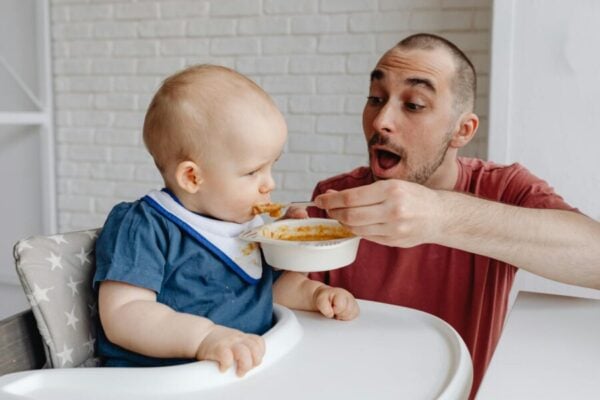 photo of a man in a red shirt feeding a baby